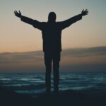 Man standing with open raised arms watching sunrise