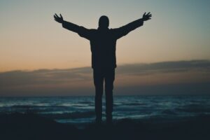 Man standing with open raised arms watching sunrise