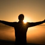 Man on edge of cliff saluting the sun at dusk