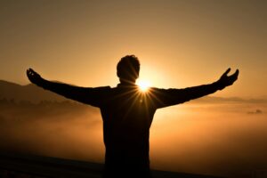 Man on edge of cliff saluting the sun at dusk